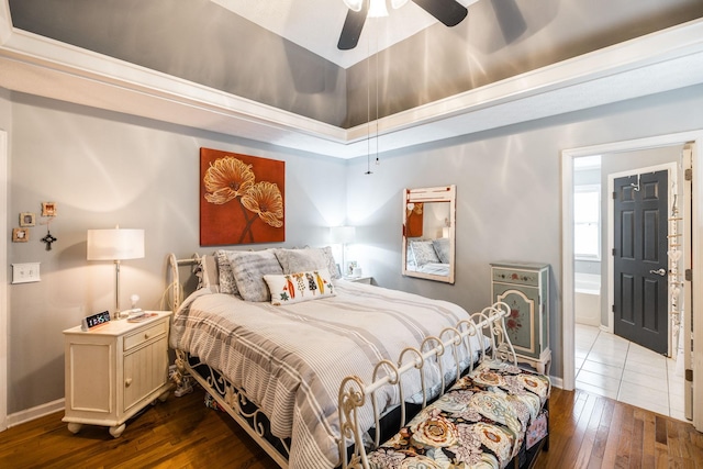 bedroom with ceiling fan, baseboards, a raised ceiling, wood-type flooring, and ensuite bath