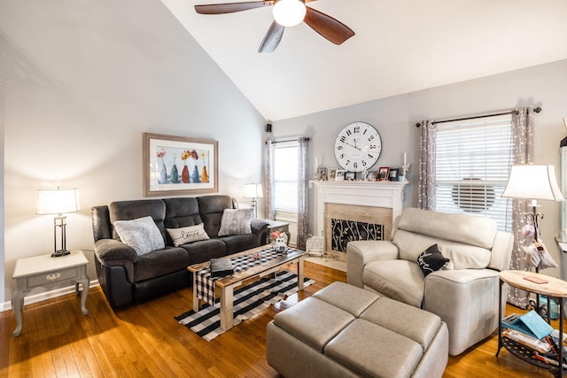 living room featuring baseboards, a ceiling fan, wood-type flooring, a fireplace with flush hearth, and high vaulted ceiling