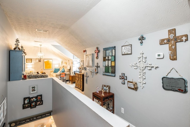 hallway with lofted ceiling, visible vents, a textured ceiling, and an upstairs landing