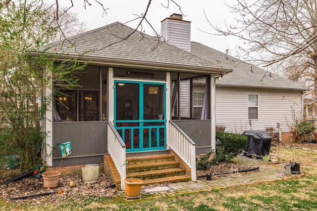 rear view of house featuring a shingled roof, a sunroom, and a chimney