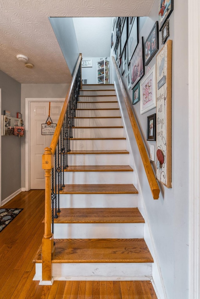 staircase featuring a textured ceiling, wood-type flooring, and baseboards