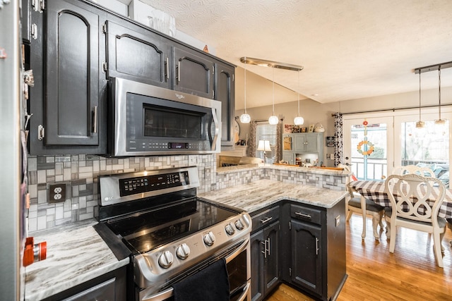 kitchen with a peninsula, appliances with stainless steel finishes, light wood-type flooring, decorative backsplash, and decorative light fixtures