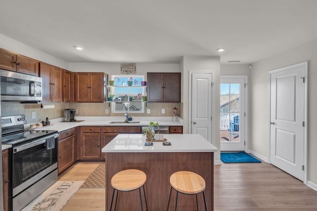 kitchen with appliances with stainless steel finishes, a kitchen breakfast bar, a center island, light countertops, and light wood-type flooring