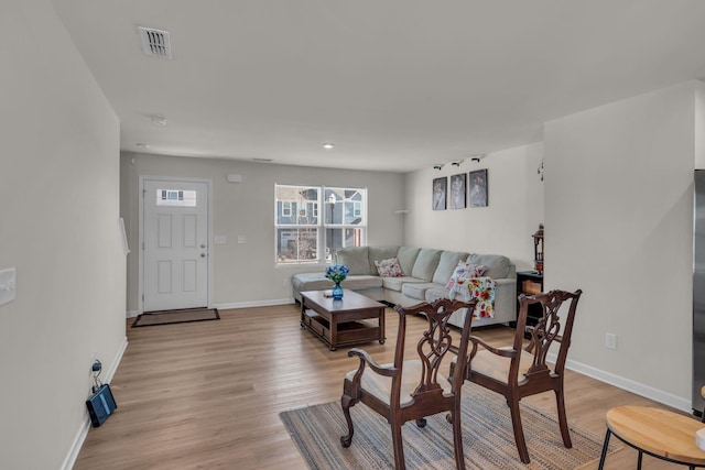 living area featuring light wood-type flooring, visible vents, and baseboards