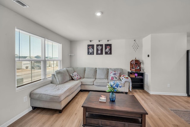 living room with light wood-type flooring, visible vents, and baseboards