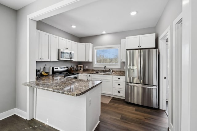 kitchen featuring dark wood finished floors, a peninsula, a sink, appliances with stainless steel finishes, and white cabinetry