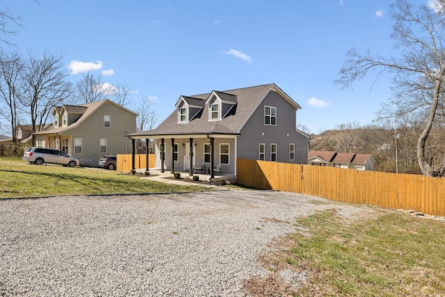 view of front of home with a porch, gravel driveway, a front lawn, and fence