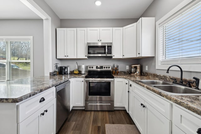 kitchen with a sink, dark wood-style floors, white cabinetry, appliances with stainless steel finishes, and a peninsula