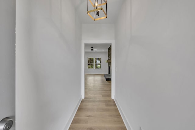 hall with a notable chandelier, light wood-style flooring, and baseboards