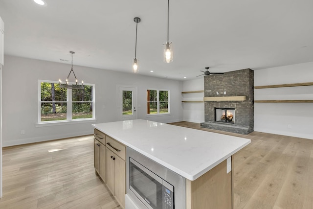 kitchen featuring decorative light fixtures, a fireplace, light wood finished floors, stainless steel microwave, and a kitchen island