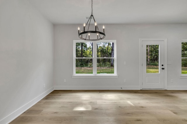 unfurnished dining area with a chandelier, light wood-type flooring, and baseboards