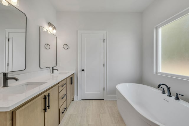 full bathroom with double vanity, a soaking tub, baseboards, and a sink