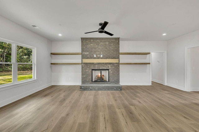 unfurnished living room featuring light wood finished floors, baseboards, visible vents, a brick fireplace, and recessed lighting