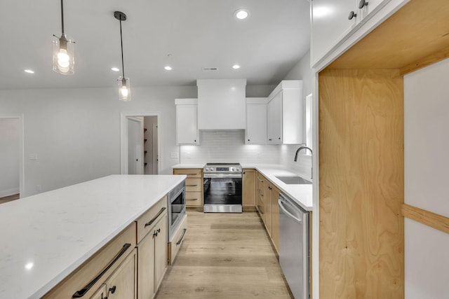 kitchen featuring stainless steel appliances, a sink, custom exhaust hood, backsplash, and light wood finished floors