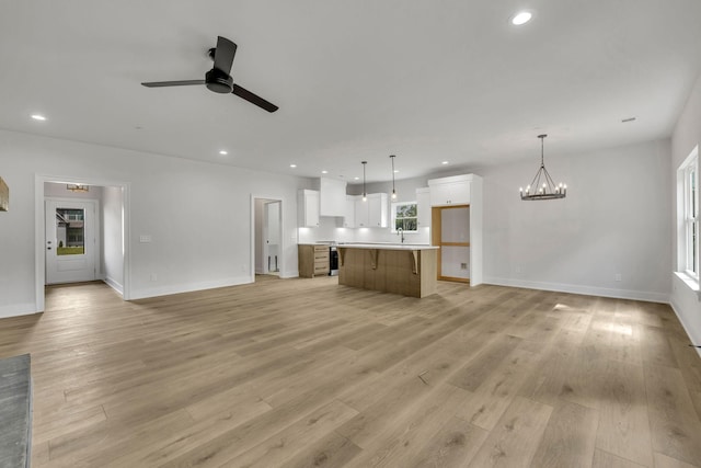 unfurnished living room featuring ceiling fan with notable chandelier, light wood-style floors, baseboards, and recessed lighting