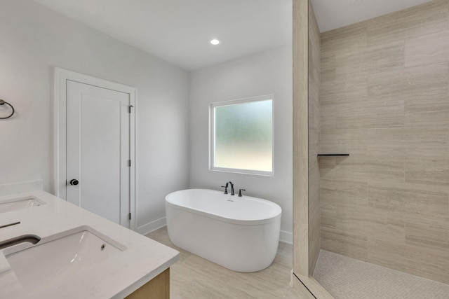 bathroom with a freestanding tub, tiled shower, a sink, and double vanity