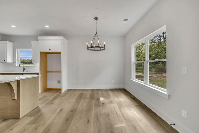 unfurnished dining area featuring light wood-type flooring, baseboards, a notable chandelier, and recessed lighting