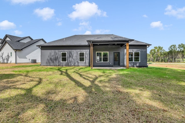 rear view of property featuring a shingled roof, a lawn, and a patio