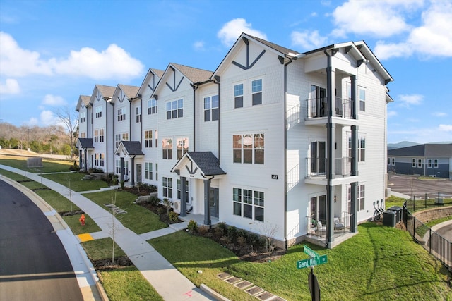 multi unit property featuring a residential view, fence, a balcony, and a front lawn