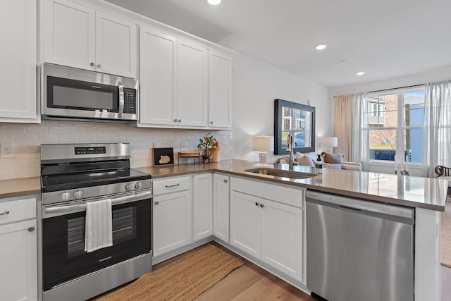 kitchen featuring a peninsula, a sink, white cabinetry, appliances with stainless steel finishes, and tasteful backsplash