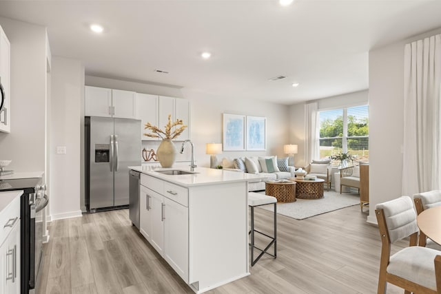 kitchen with a breakfast bar, a sink, white cabinets, appliances with stainless steel finishes, and light wood-type flooring