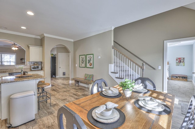 dining space featuring stairway, light wood-style flooring, arched walkways, ceiling fan, and crown molding