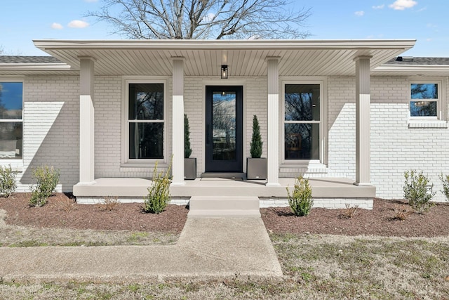 doorway to property featuring covered porch and brick siding