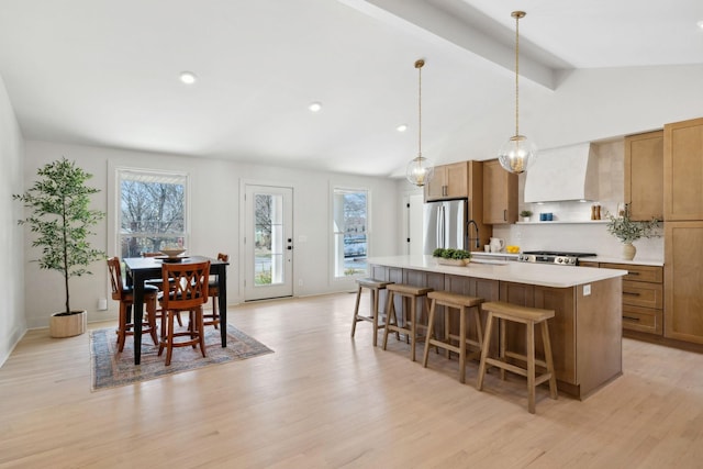 kitchen with light wood-style flooring, custom exhaust hood, freestanding refrigerator, an island with sink, and a kitchen bar