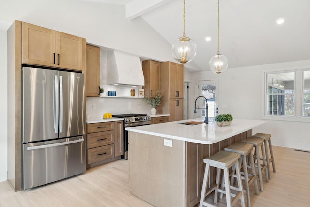 kitchen with vaulted ceiling with beams, a sink, light wood-style floors, appliances with stainless steel finishes, and wall chimney exhaust hood