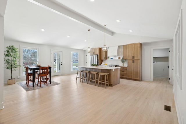 kitchen with a kitchen island, visible vents, wall chimney range hood, light wood-type flooring, and freestanding refrigerator