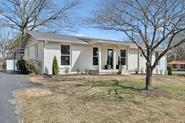 view of front facade featuring a porch, an outbuilding, brick siding, and a front lawn