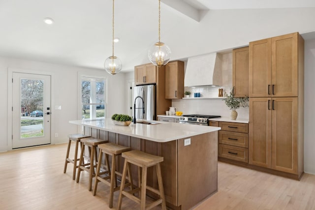 kitchen featuring light wood-style flooring, a kitchen island with sink, stainless steel appliances, light countertops, and wall chimney range hood