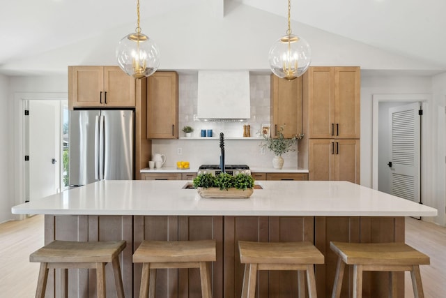 kitchen with lofted ceiling, a kitchen island with sink, light wood-style floors, light countertops, and freestanding refrigerator