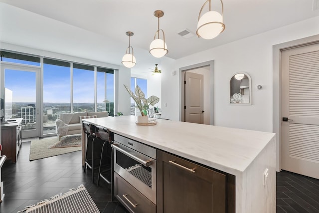 kitchen with open floor plan, light countertops, dark brown cabinets, a wall of windows, and pendant lighting