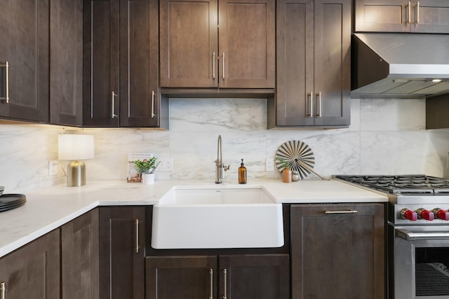 kitchen featuring light countertops, a sink, wall chimney range hood, dark brown cabinets, and high end range