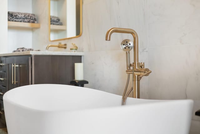 full bath featuring tile walls, a freestanding tub, and vanity