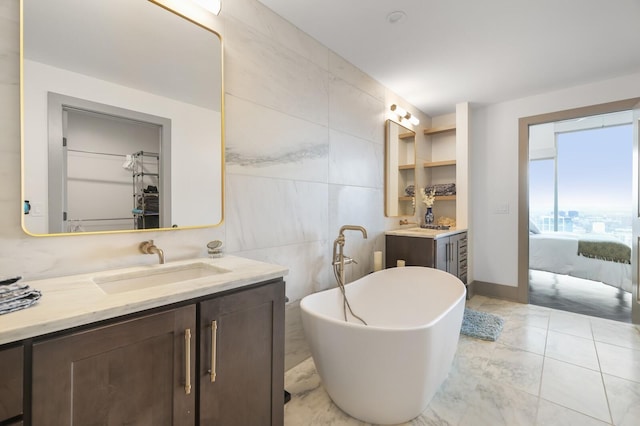 ensuite bathroom with vanity, tile walls, a freestanding bath, a spacious closet, and ensuite bath