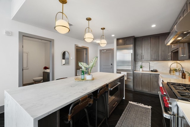 kitchen with high end appliances, tasteful backsplash, a sink, a kitchen island, and under cabinet range hood