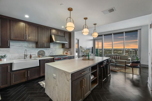 kitchen featuring visible vents, high end range, a sink, dark brown cabinets, and under cabinet range hood