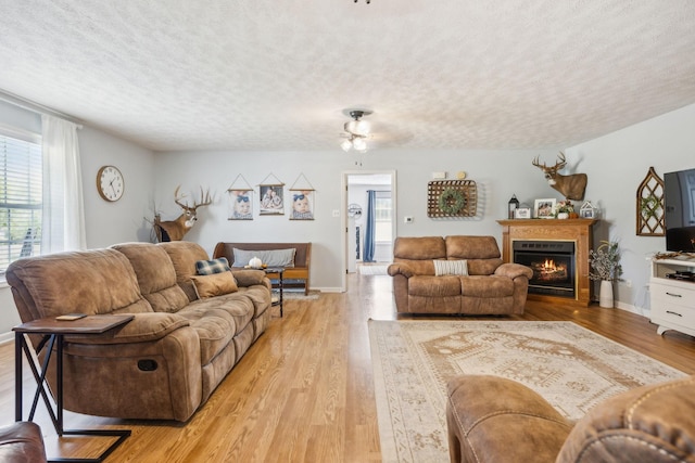 living room featuring a textured ceiling, a lit fireplace, light wood finished floors, and baseboards