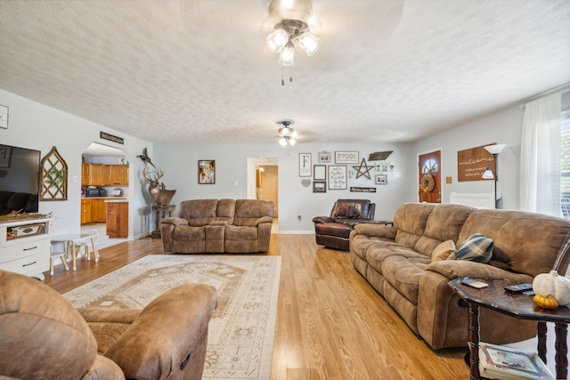 living area with light wood-style floors, arched walkways, a textured ceiling, and a ceiling fan