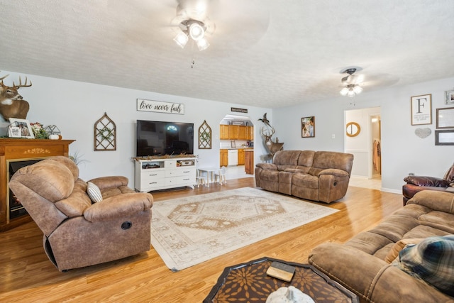 living area with ceiling fan, a textured ceiling, wood finished floors, and baseboards