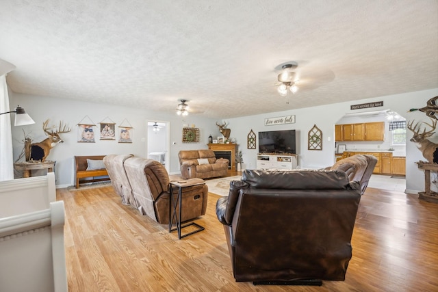 living area featuring a fireplace, light wood finished floors, a ceiling fan, a textured ceiling, and baseboards