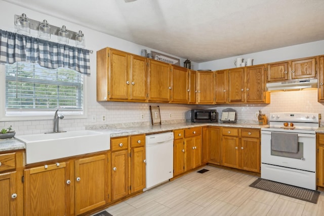 kitchen with white appliances, brown cabinetry, light countertops, under cabinet range hood, and a sink