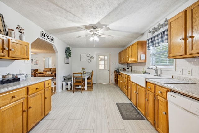 kitchen featuring arched walkways, dishwasher, ceiling fan, light countertops, and a sink