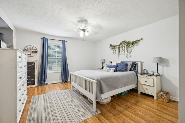 bedroom featuring light wood-style flooring, baseboards, ceiling fan, and a textured ceiling