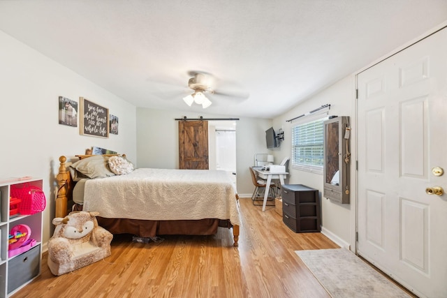 bedroom featuring light wood-style floors, a barn door, baseboards, and ceiling fan