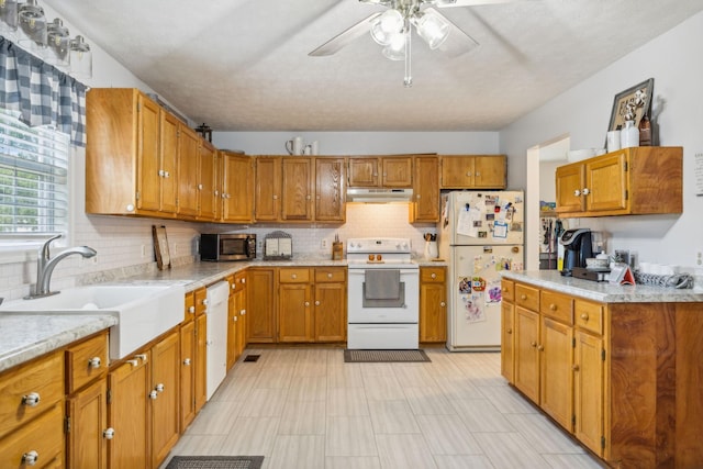 kitchen with brown cabinets, white appliances, a sink, and under cabinet range hood