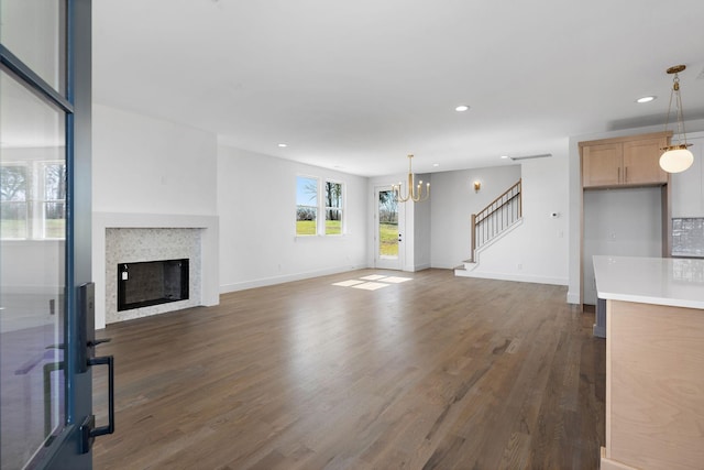 unfurnished living room featuring dark wood-type flooring, stairway, recessed lighting, a fireplace, and an inviting chandelier