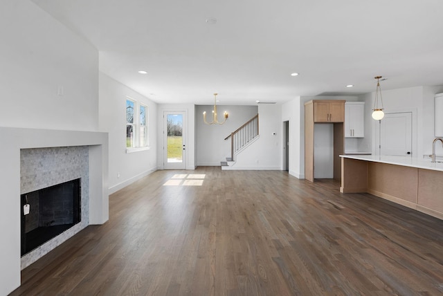 unfurnished living room featuring baseboards, stairs, a fireplace, a notable chandelier, and dark wood-style flooring